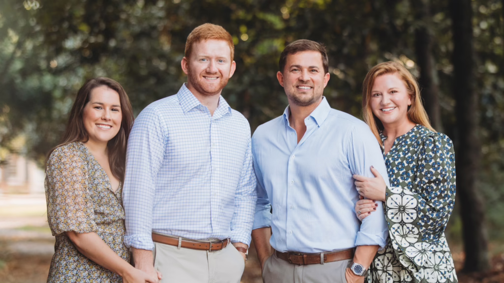 Four adults standing outdoors in a park, smiling at the camera.